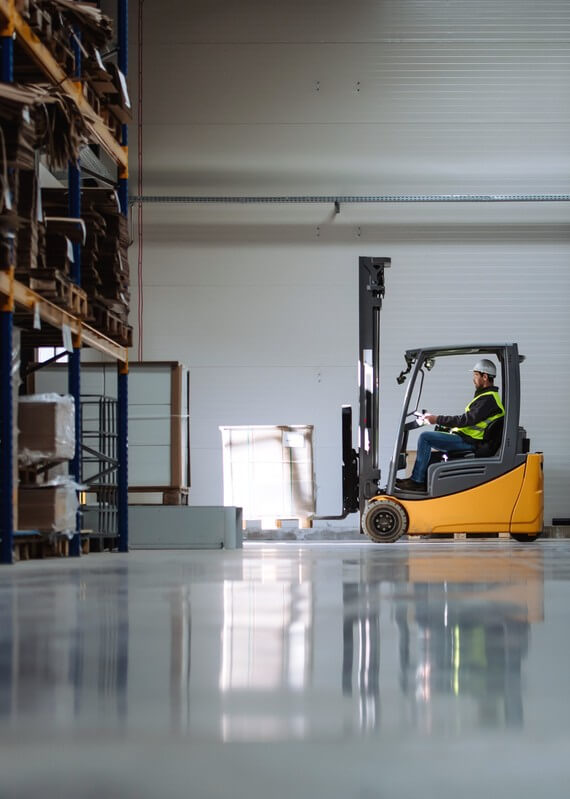 Side view of forklift in warehouse with male driver.